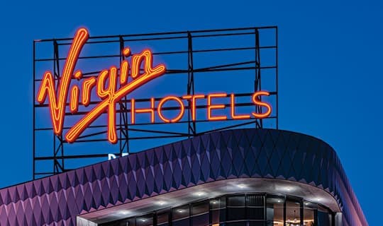Geometric hotel architecture with neon rooftop identity signage.